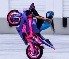 a person on a pink and blue motorcycle doing a wheelie