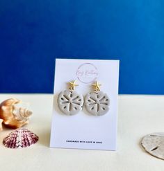 Bring a touch of beach side charm to your style with these exquisite sand dollar earrings. Each pair is handcrafted from lightweight polymer clay and set on a hypoallergenic, nickel-free gold plated starfish post. These earrings are perfect for adding a hint of summer elegance to any outfit. They also make a thoughtful gift for the beach lover in your life.  As with all handmade items, small imperfections, variations in color and size are possible. This is inherent to the nature and charm of han Beach Earrings Summer, Sand Dollar Earrings, Neutral Earrings, Summer Elegance, Earrings Beach, Beach Side, Beach Earrings, Earrings Summer, Beach Lover