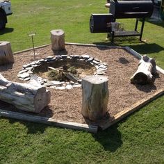 an outdoor fire pit made out of logs in the middle of some grass and dirt