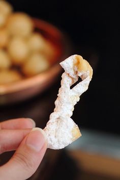 a hand holding up a piece of food in front of a bowl full of other food