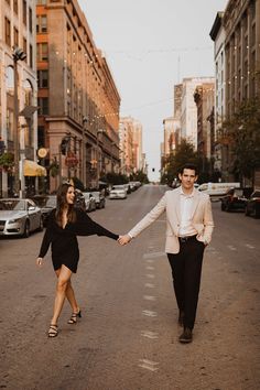 a man and woman holding hands while walking down the street in front of tall buildings