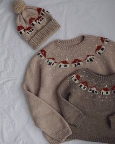 two knitted sweaters and hat are laying on a white sheet in the bed