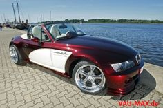 a red and white convertible car parked next to the water