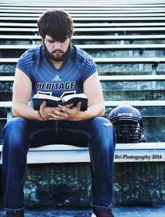 a man is sitting on the bleachers reading a book while holding a football helmet