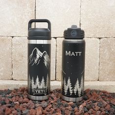 two stainless steel water bottles sitting next to each other on top of rocks and gravel