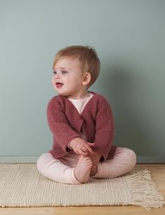 a baby sitting on the floor wearing a sweater