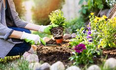 a woman kneeling down in the grass with gardening gloves on and potted plants next to her