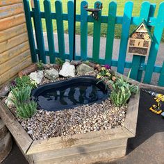 a small pond in the middle of a garden with rocks and gravel around it, next to a fence