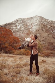 a man holding a baby in his arms while standing on top of a dry grass field