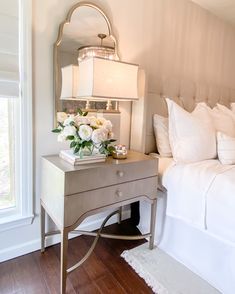 a bedroom with a bed, nightstand and flowers on the night stand in front of it