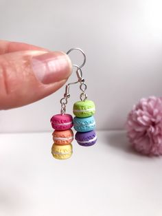 a person is holding three small macaroni and cheese earrings in front of a pink flower