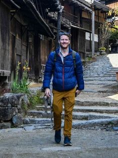 a man in blue jacket walking down street next to wooden building with stairs and steps