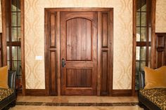 a wooden door sitting inside of a living room next to two couches on top of a tiled floor