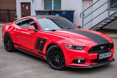 a red mustang with black stripes parked in front of a building on the side of a street