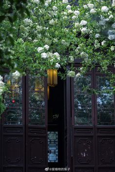 an open door to a building with flowers on the outside and trees growing over it