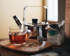 a cup of tea sitting on top of a wooden cutting board next to a kettle