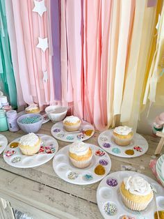 cupcakes are on plates in front of colorful curtains