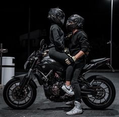 two people sitting on a motorcycle in the dark with their helmets on and looking at something