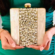 a woman in a green dress is holding a gold and white purse with lots of beads on it