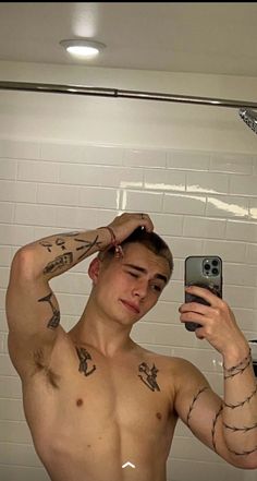 a shirtless man taking a selfie in the bathroom with his cell phone and tattoos on his arm