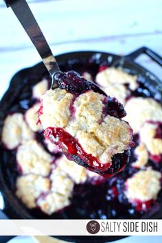 blueberry cobbler in a cast iron skillet being lifted with a ladle