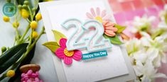 a birthday card with flowers and the number 22 on it, sitting next to some flowers