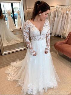 a woman standing in front of a mirror wearing a white wedding dress with long sleeves