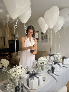 a woman standing in front of a table filled with white balloons and gift wrapped presents