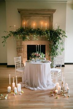 a table with candles and flowers on it in front of a fire place surrounded by chairs