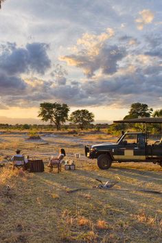 people are sitting on the grass in front of an open field with a safari vehicle