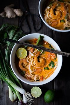 two bowls filled with noodles and vegetables on top of a wooden table next to chopsticks