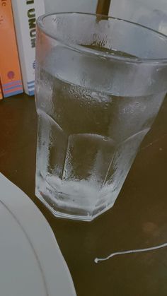 a glass filled with water sitting on top of a table next to a white plate