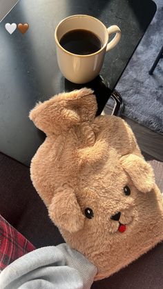 a brown teddy bear sitting on top of a table next to a cup of coffee