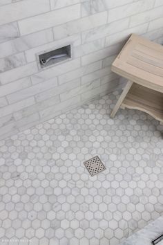 a bathroom with white hexagonal tiles and a wooden bench on the floor next to it