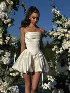 a woman in a short white dress walking down a runway with flowers on the side