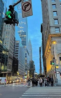 people crossing the street at an intersection with traffic lights and skyscrapers in the background