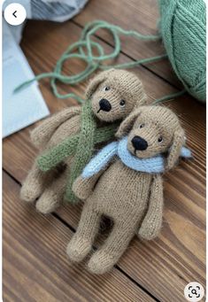 two knitted teddy bears sitting on top of a wooden floor next to balls of yarn