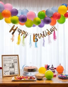 a birthday party with balloons, cake and confetti on a table in front of a window