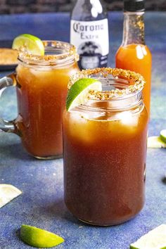 two glasses filled with drinks sitting on top of a blue table next to limes