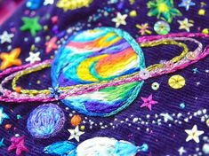 a close up view of an embroidered space scene with stars, planets and the sun