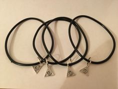 four black leather bracelets with silver charms on white background, one has an eye charm and the other has a triangle pendant