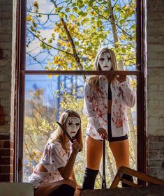 two women with painted faces are standing in front of a window and one is holding a stick