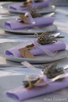 purple napkins with lavender flowers tied to them are sitting on white plates and silverware