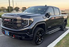 a large black truck parked in a parking lot next to a grass covered park area