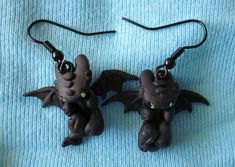 two small black dragon shaped earrings on a blue cloth covered table with a pair of dangling earwires