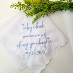 a white handkerchief with blue writing on it next to a bouquet of flowers and greenery