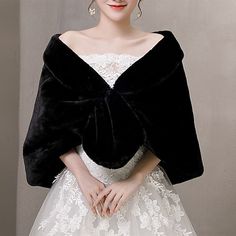 a woman wearing a black and white wedding cape with lace on the bottom, in front of a gray wall