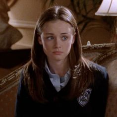 a woman with long brown hair wearing a black sweater and white shirt is sitting on a couch