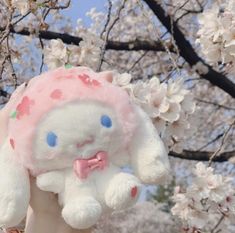 a hand holding a stuffed animal in front of cherry blossom trees