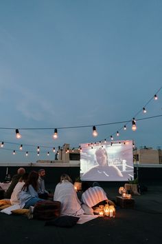 people sitting on the ground watching a movie at night with candles lit up in front of them